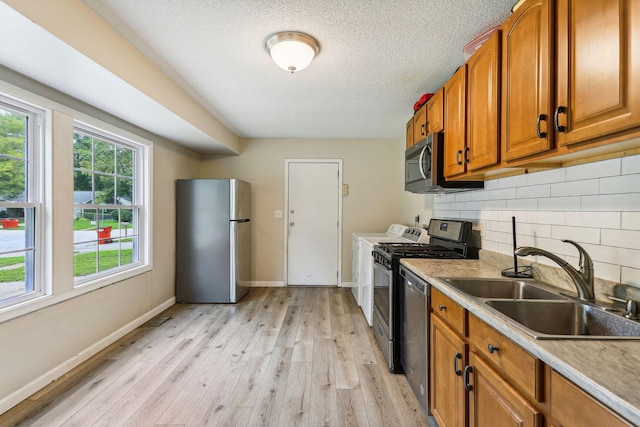 kitchen featuring sink, appliances with stainless steel finishes, tasteful backsplash, light hardwood / wood-style floors, and a textured ceiling