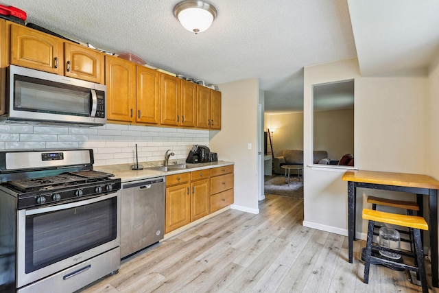 kitchen with appliances with stainless steel finishes, tasteful backsplash, sink, light wood-type flooring, and a textured ceiling