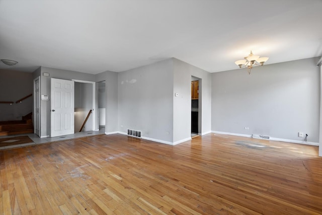 spare room with a notable chandelier and light wood-type flooring