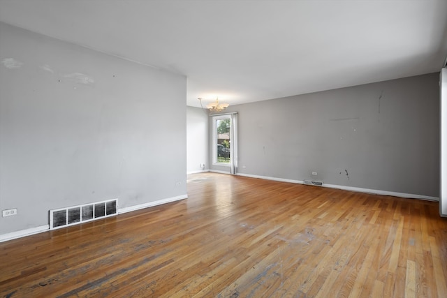 spare room with an inviting chandelier and hardwood / wood-style flooring