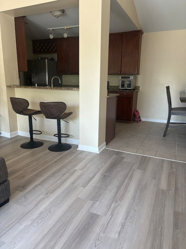 kitchen featuring lofted ceiling, track lighting, light hardwood / wood-style flooring, and stainless steel refrigerator