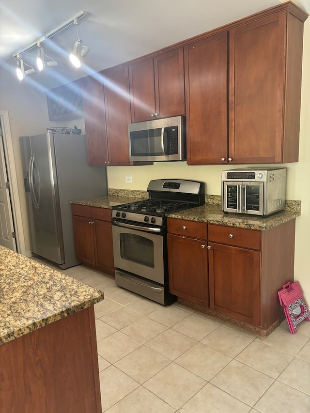 kitchen featuring track lighting, light tile patterned flooring, stainless steel appliances, and dark stone countertops