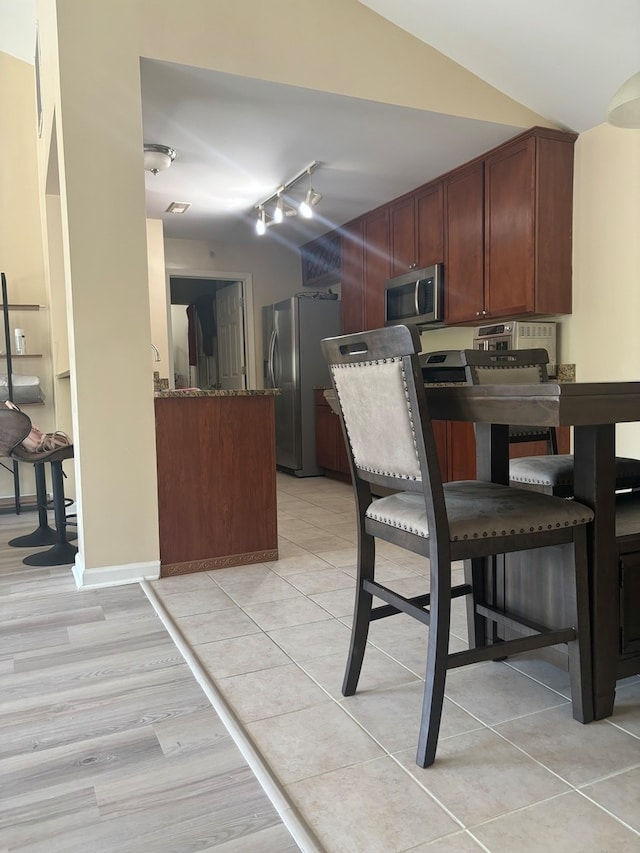 kitchen featuring lofted ceiling, dark stone counters, track lighting, light hardwood / wood-style floors, and appliances with stainless steel finishes