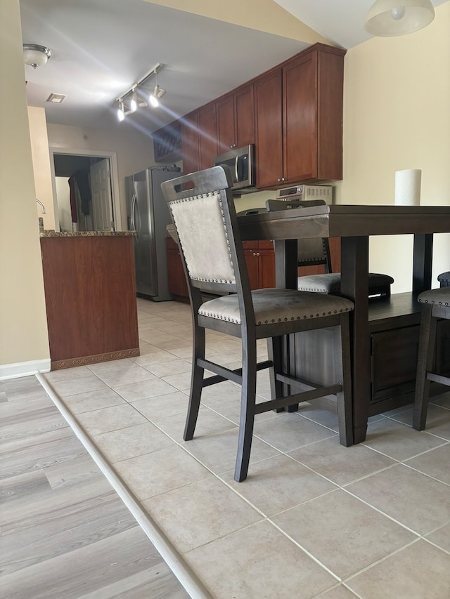 kitchen featuring appliances with stainless steel finishes, light hardwood / wood-style flooring, dark stone countertops, and track lighting