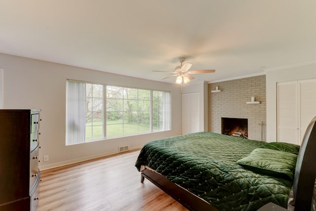 bedroom with ornamental molding, light hardwood / wood-style flooring, a brick fireplace, and ceiling fan