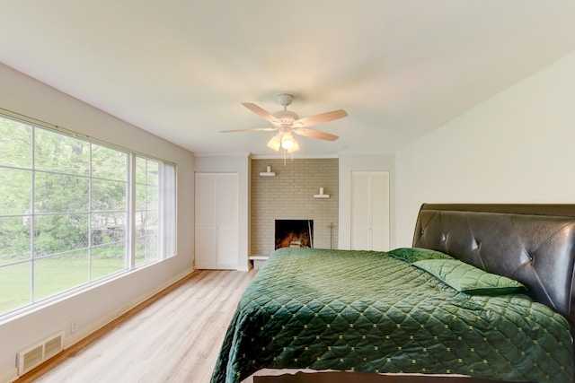 bedroom with ceiling fan, brick wall, a brick fireplace, and light hardwood / wood-style floors