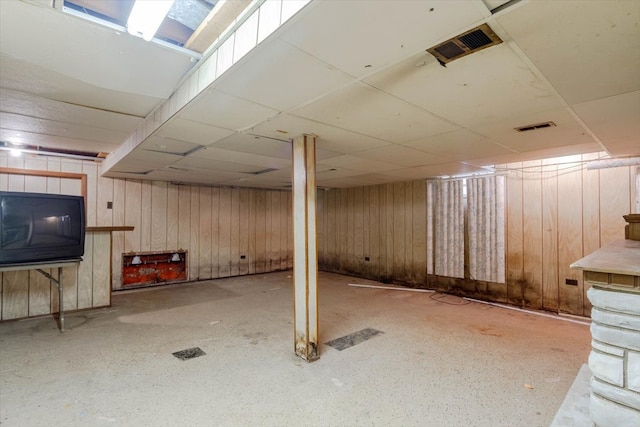 basement featuring wood walls and a drop ceiling