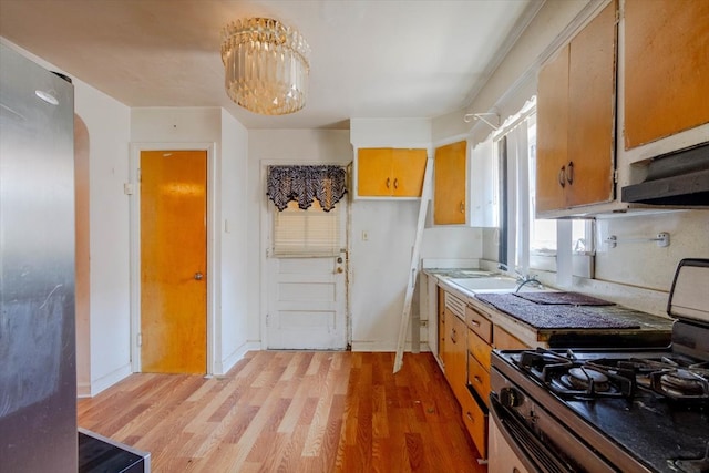 kitchen featuring black range oven, sink, exhaust hood, an inviting chandelier, and light hardwood / wood-style floors