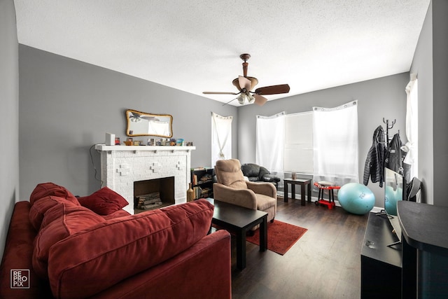 living room with ceiling fan, dark hardwood / wood-style floors, a brick fireplace, and a textured ceiling