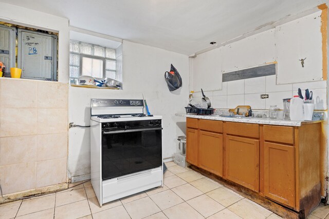 kitchen with backsplash, white gas range oven, light tile patterned floors, and tile walls