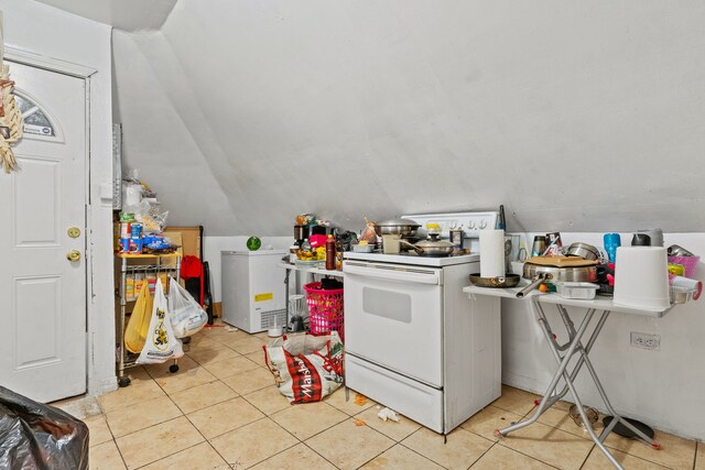 kitchen with white electric stove, light tile patterned floors, and vaulted ceiling