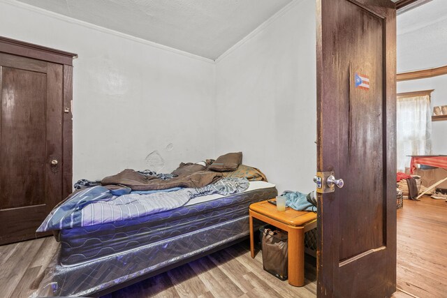 bedroom with ornamental molding, light hardwood / wood-style flooring, and a textured ceiling