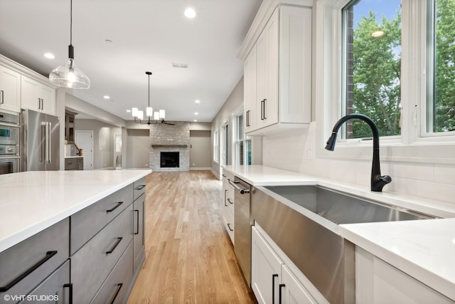 kitchen with light hardwood / wood-style flooring, stainless steel appliances, white cabinets, a stone fireplace, and hanging light fixtures