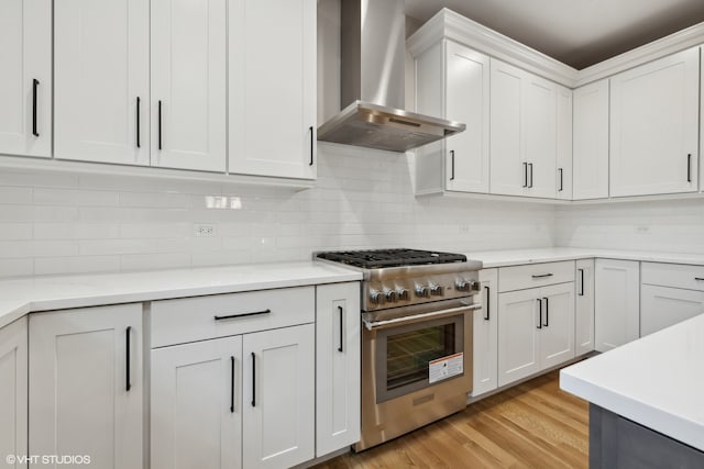 kitchen with stainless steel range, white cabinetry, light hardwood / wood-style flooring, wall chimney range hood, and backsplash