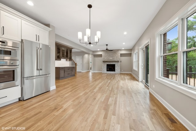 kitchen with white cabinetry, a chandelier, light wood-type flooring, stainless steel appliances, and a fireplace