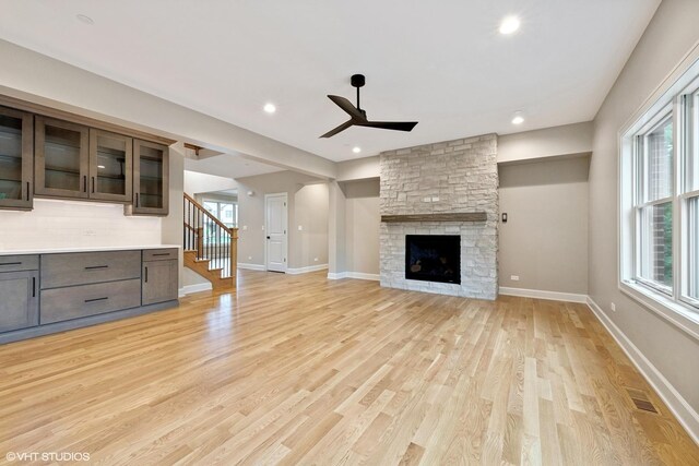 unfurnished living room with a stone fireplace, light wood-type flooring, and ceiling fan