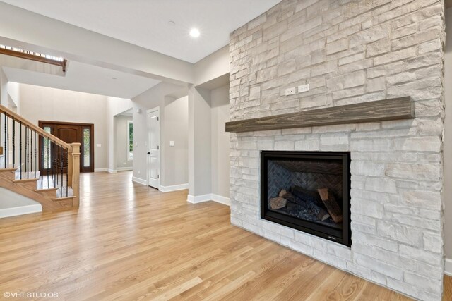 unfurnished living room featuring a stone fireplace and light wood-type flooring