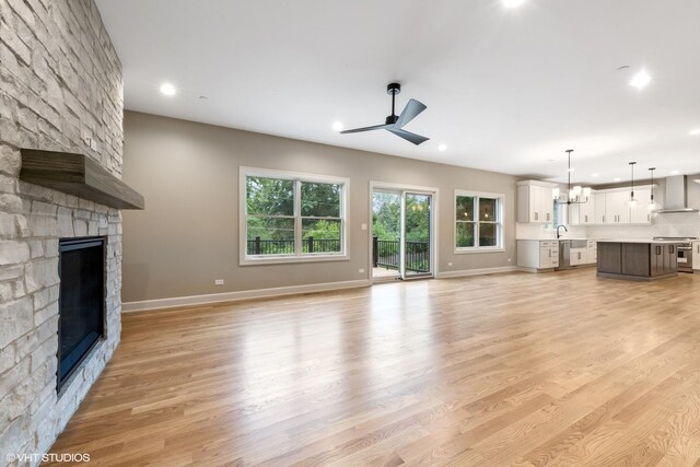 unfurnished living room with a stone fireplace, ceiling fan with notable chandelier, light hardwood / wood-style flooring, and sink