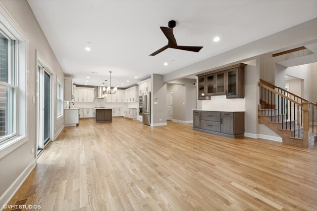 unfurnished living room featuring sink, ceiling fan with notable chandelier, and light hardwood / wood-style flooring