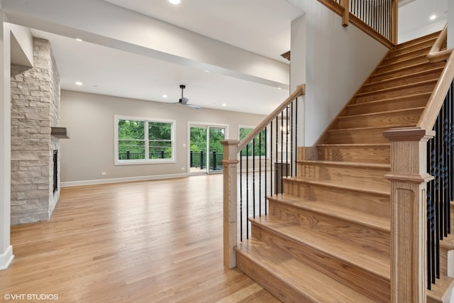 staircase featuring ceiling fan, a fireplace, and light hardwood / wood-style flooring