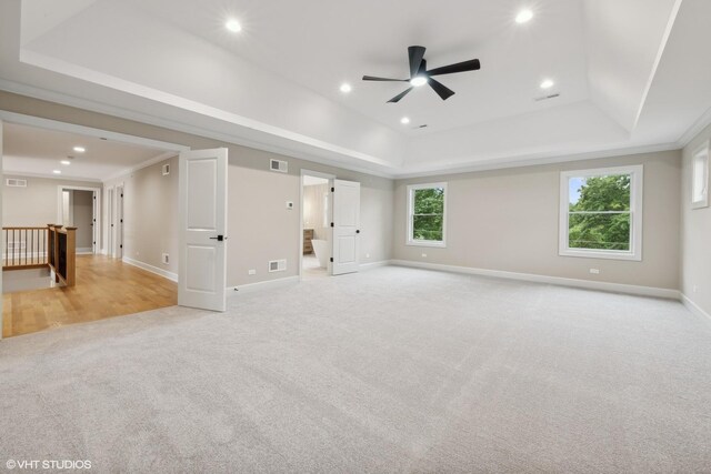 unfurnished living room with crown molding, a tray ceiling, and light colored carpet