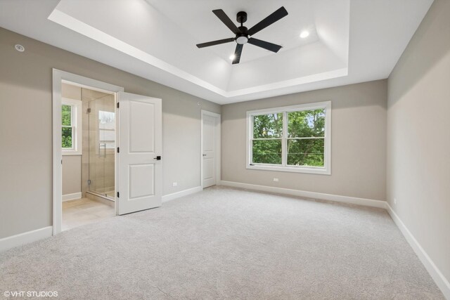 unfurnished bedroom with light carpet, ensuite bathroom, and a raised ceiling