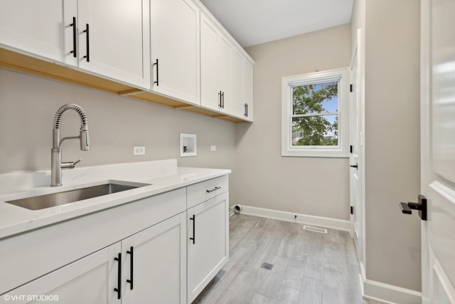 laundry room featuring sink, light wood-type flooring, cabinets, and hookup for a washing machine