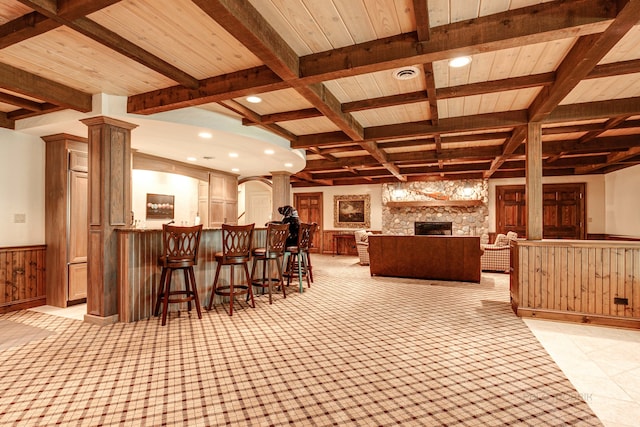 interior space featuring a stone fireplace, indoor bar, ornate columns, beam ceiling, and coffered ceiling