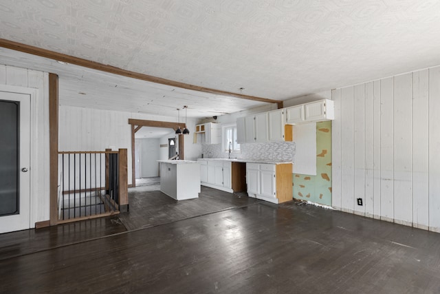 interior space featuring white cabinets, wooden walls, dark wood-type flooring, and pendant lighting