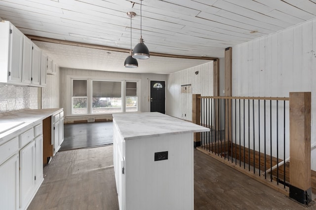 kitchen with dark wood-type flooring, a center island, pendant lighting, white cabinets, and wood walls