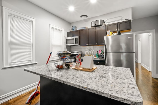 kitchen with backsplash, light stone countertops, a kitchen island, dark brown cabinetry, and stainless steel appliances