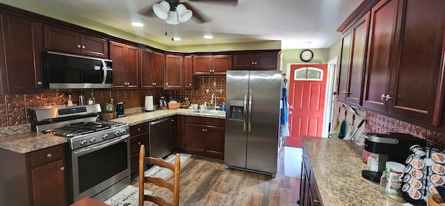 kitchen with sink, dark hardwood / wood-style floors, decorative backsplash, appliances with stainless steel finishes, and light stone counters