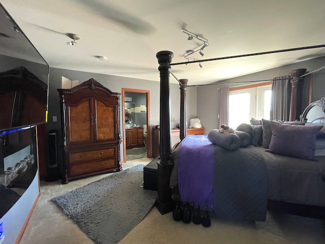 carpeted bedroom with track lighting, lofted ceiling, and ensuite bathroom