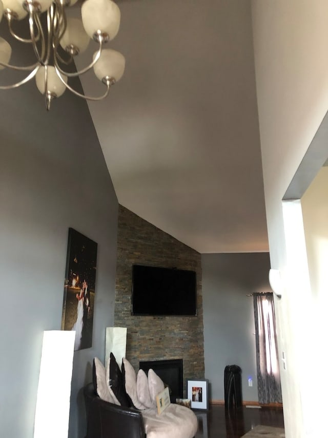 living room featuring vaulted ceiling, a chandelier, and a stone fireplace