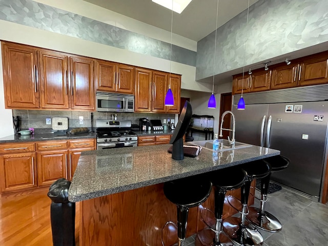 kitchen featuring appliances with stainless steel finishes, dark stone countertops, pendant lighting, a kitchen island with sink, and sink