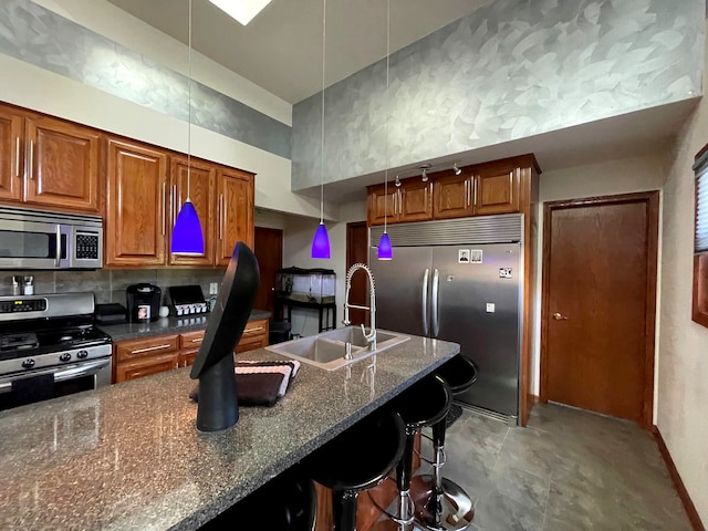 kitchen featuring appliances with stainless steel finishes, a breakfast bar, pendant lighting, dark stone counters, and sink