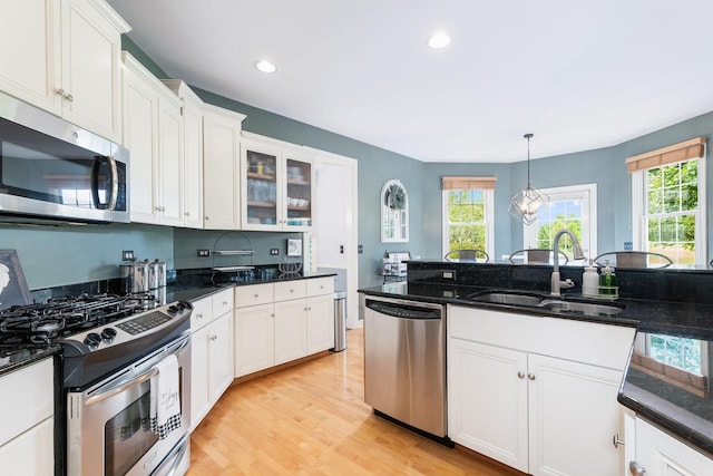 kitchen with a sink, white cabinets, hanging light fixtures, appliances with stainless steel finishes, and glass insert cabinets