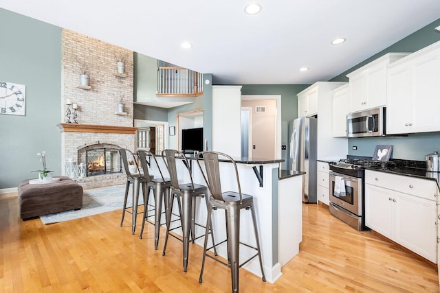 kitchen featuring appliances with stainless steel finishes, light wood-style floors, open floor plan, white cabinetry, and a kitchen breakfast bar