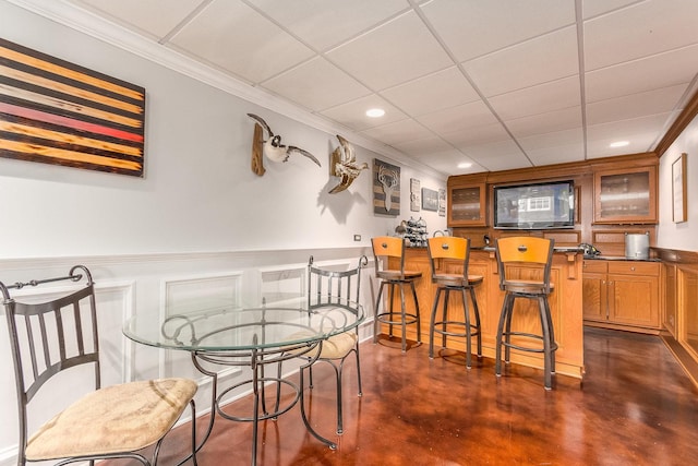 dining area with crown molding, a paneled ceiling, recessed lighting, a bar, and concrete floors