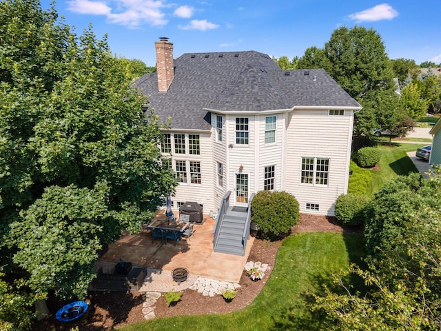 back of property with a patio area, a shingled roof, a chimney, and a lawn