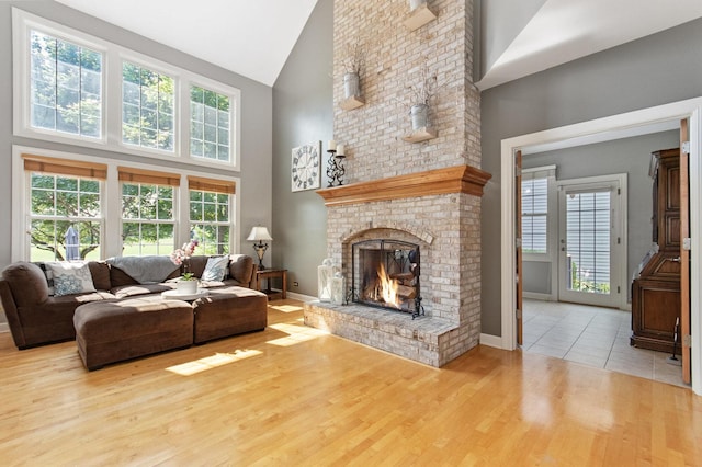 living room with high vaulted ceiling, light wood-type flooring, a brick fireplace, and baseboards