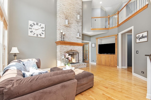 living area with a high ceiling, a brick fireplace, wood finished floors, and baseboards