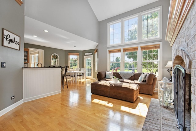 living area with high vaulted ceiling, light wood-style flooring, recessed lighting, baseboards, and a brick fireplace