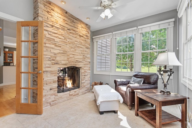 living room with light tile patterned floors, a stone fireplace, and a ceiling fan