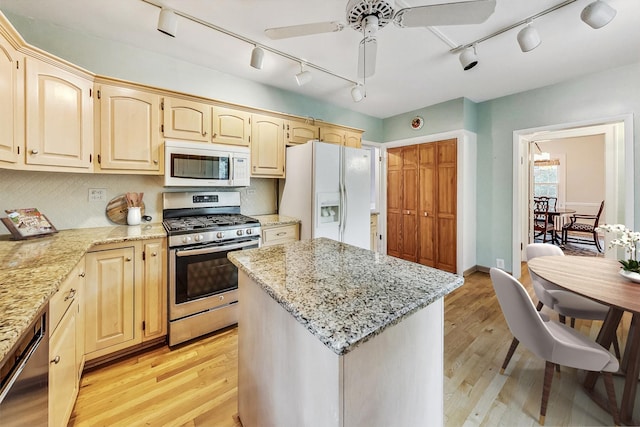 kitchen with appliances with stainless steel finishes, light stone counters, ceiling fan, light hardwood / wood-style flooring, and a kitchen island