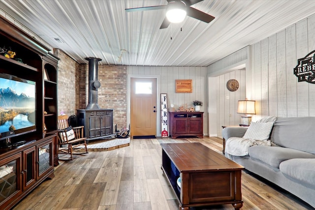 living room featuring brick wall, light wood-type flooring, ceiling fan, and a wood stove