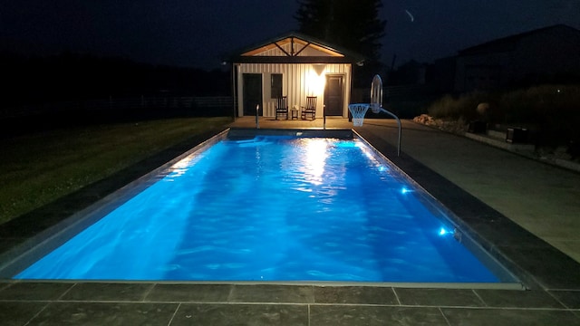 pool at twilight with an outbuilding and a patio area