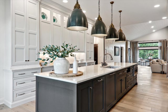 kitchen featuring pendant lighting, sink, a kitchen island with sink, light stone counters, and white cabinets