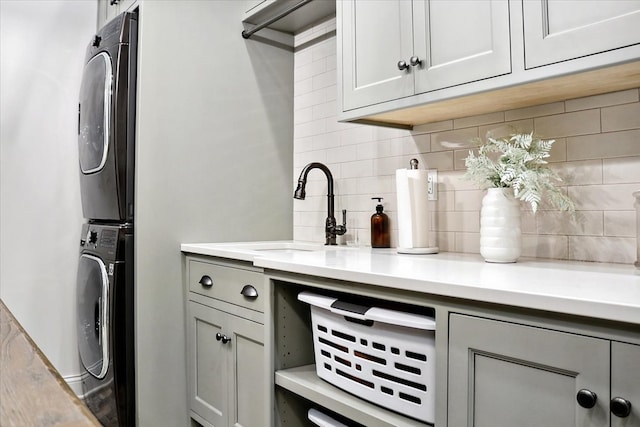 clothes washing area featuring cabinets, stacked washing maching and dryer, and sink