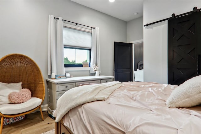 bedroom with a barn door and light hardwood / wood-style floors